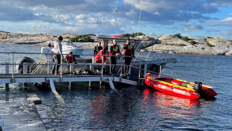 People stand on a marina next to an orange inflatable boat