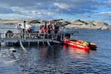 People stand on a marina next to an orange inflatable boat