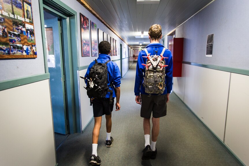 Nathaniel and Cale walking down the school corridors wearing their backpacks with drones strapped to the back.