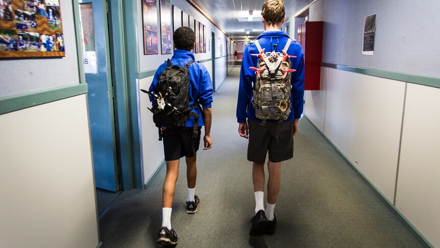 Nathaniel and Cale walking down the school corridors wearing their backpacks with drones strapped to the back.