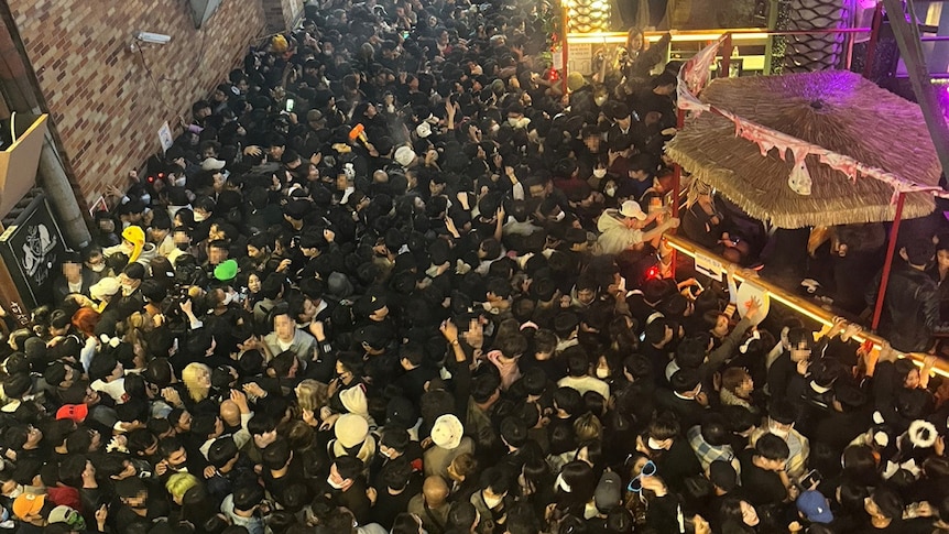 A huge crowd of people in a very narrow alleyway at night 