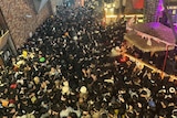 A huge crowd of people in a very narrow alleyway at night 