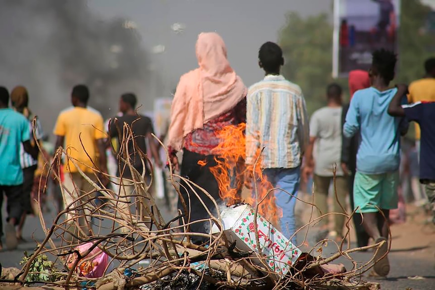 Burning barricade in foreground, with people walking away in the background.