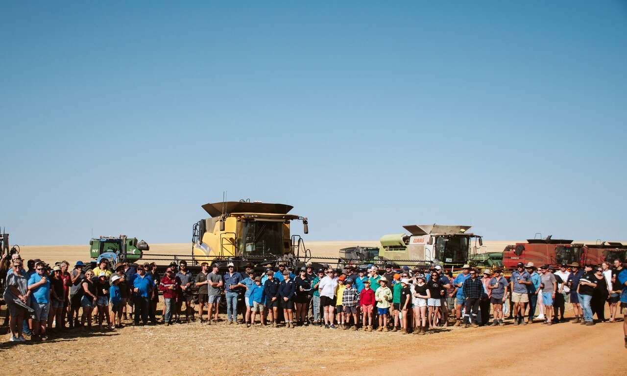 Dozens of people lined up in front of harvesters in a paddock