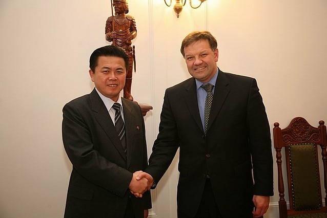 Kim Pyong-il shaking hands and smiling with Polish diplomat Mariusz Handzlik