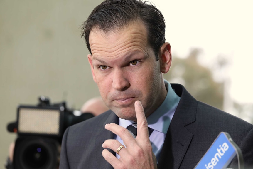 Nationals Senator Matt Canavan listening to media, eyebrows raised finger at mouth at Senate doors Parliament House