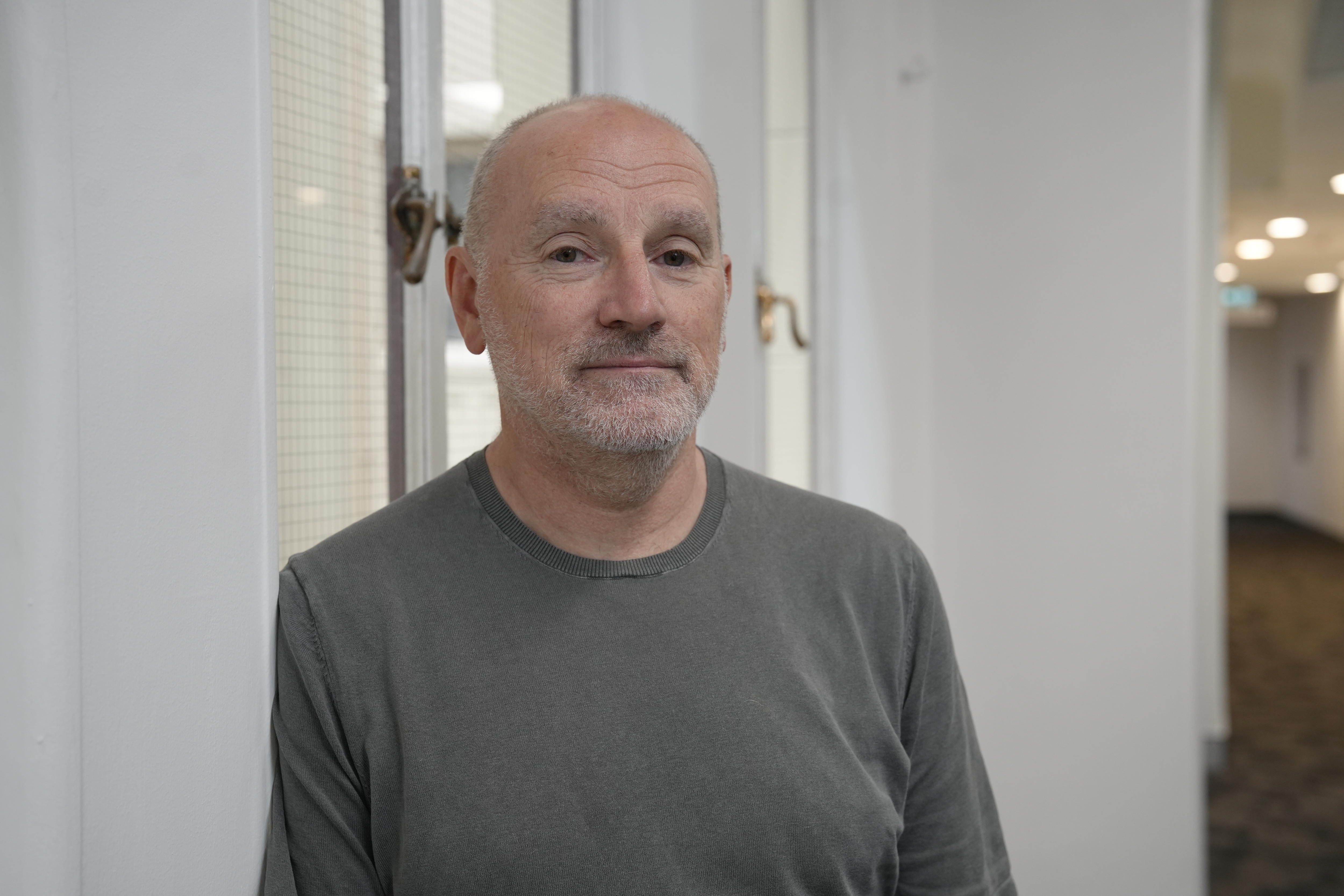 Homem olhando para a câmera encostado na parede.