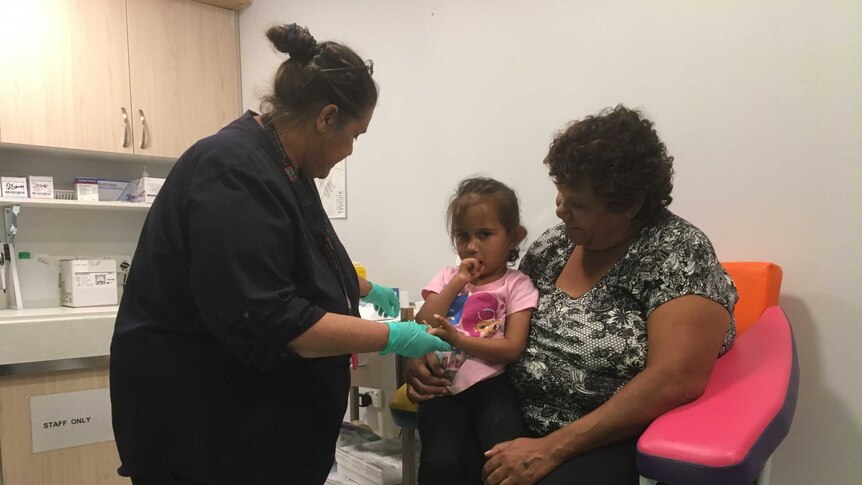 Shaventi Kelly-Harris is held by her nan as the nurse prepares her for a blood test.