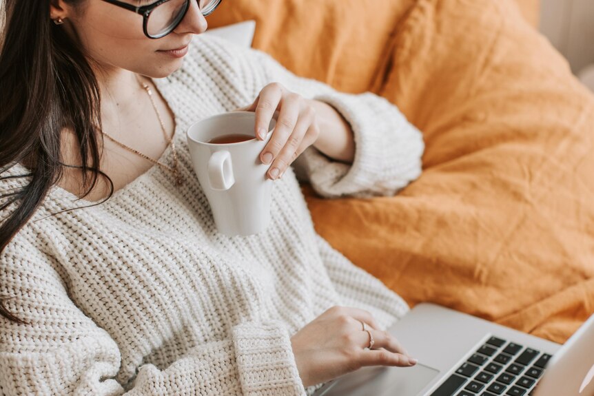 Woman browsing laptop while drinking tea