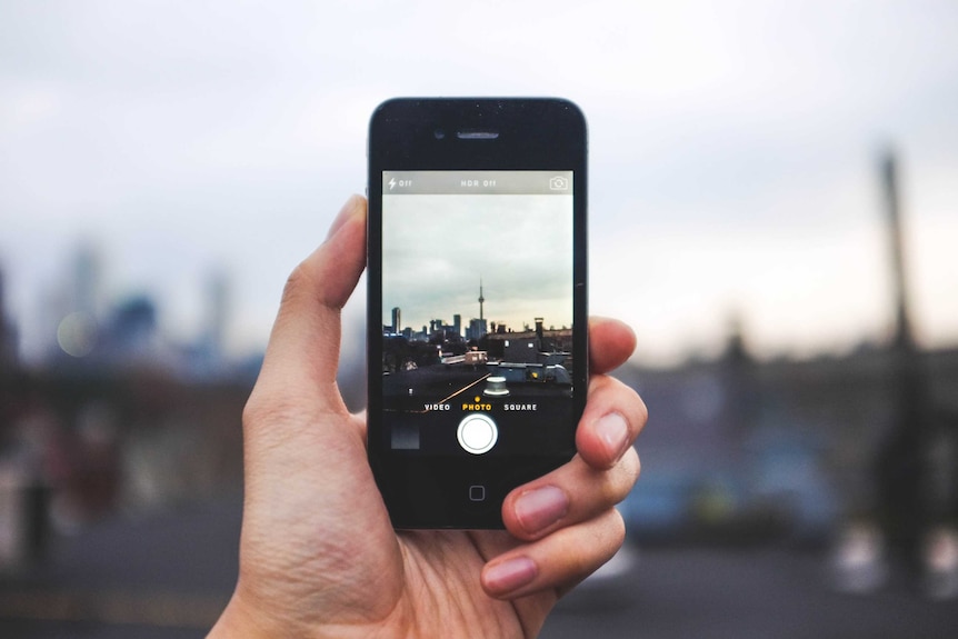 A stock image shows a person taking a photo with an iPhone.