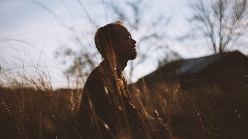 A young man sits outside meditating in a field of long gold grass