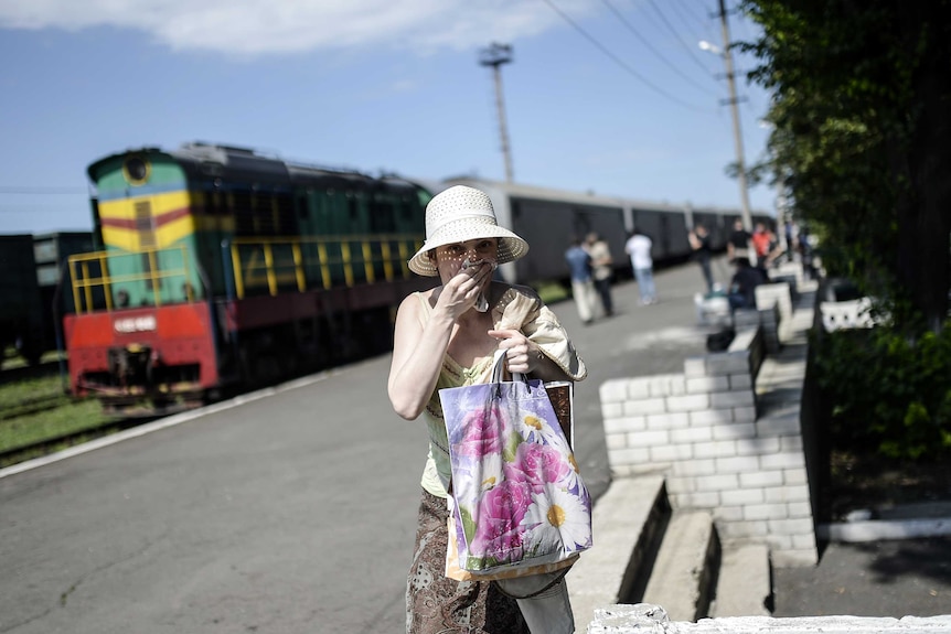 A woman covers her mouth with a piece of fabric to protect herself from the smell near train carriages filled with bodies