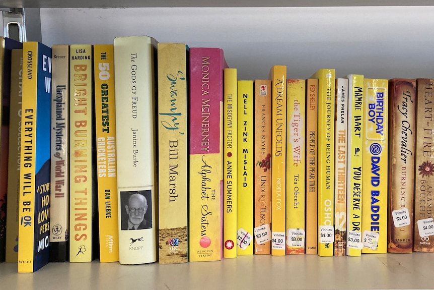 A shelf of books containing yellow spines, stacked up together at an op shop