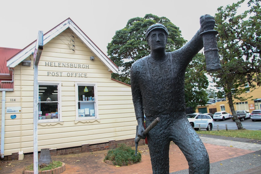 A scuplture of a miner stands in front of a post office. 