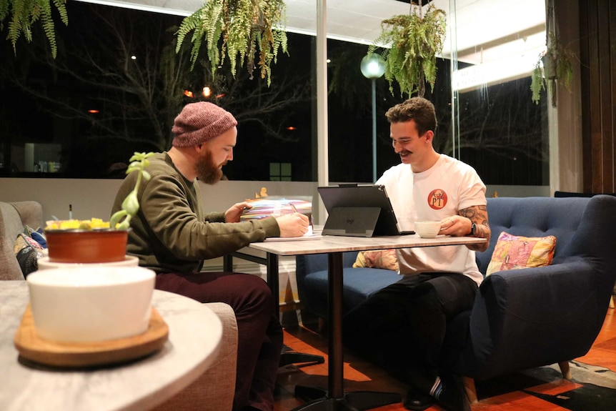 Zach and Aidan sit on couches writing and looking at a laptop.