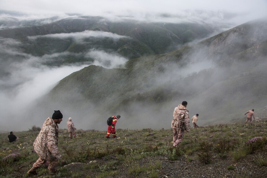 Rescue workers walk on a foggy mountain with more mountain ranges in the distance