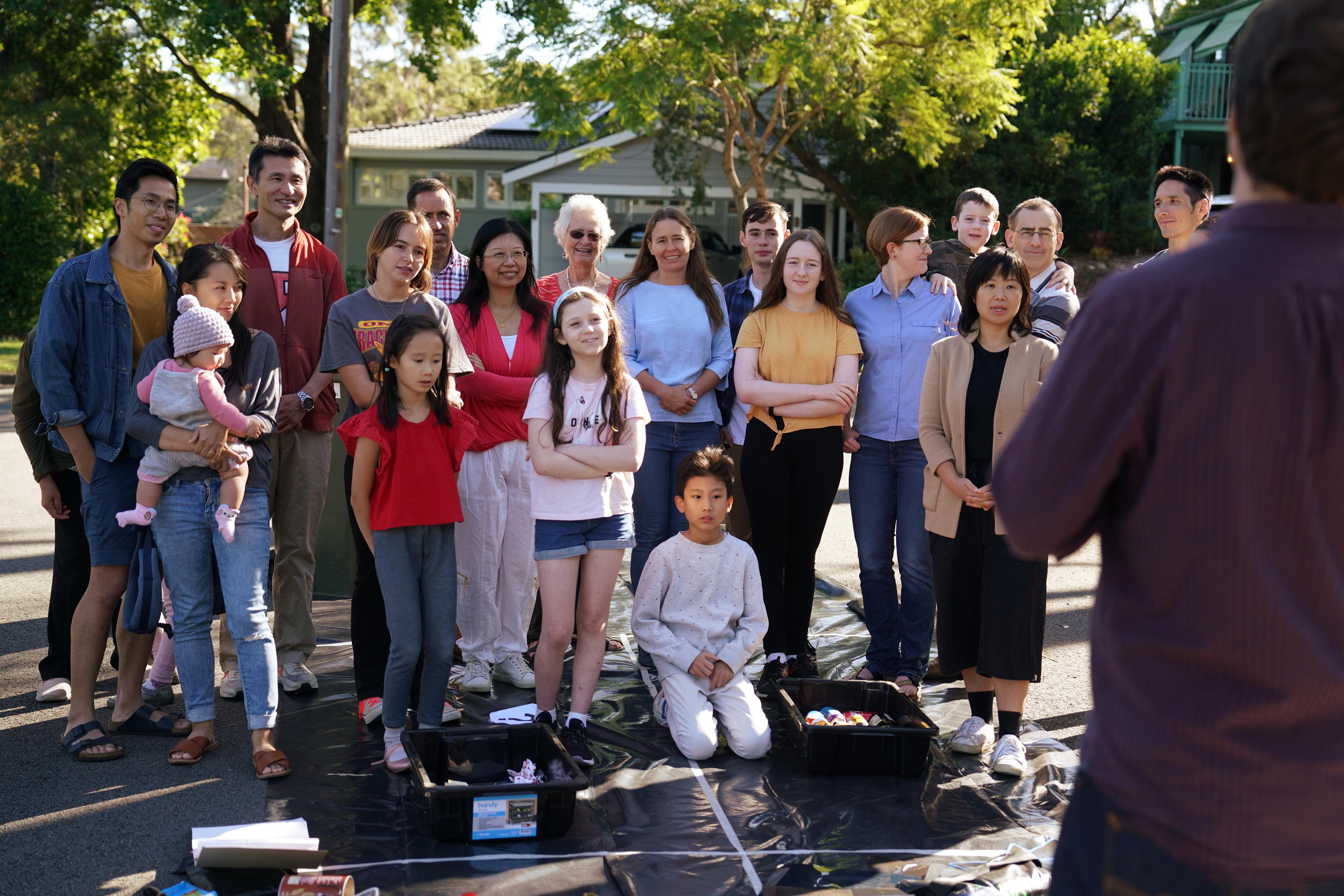 Group of men, women and children standing in a street listening to man talking to them.
