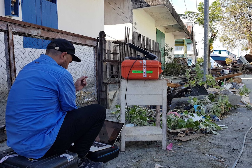 Hemingway with equipment and laptop set up in street surrounded by rubble.