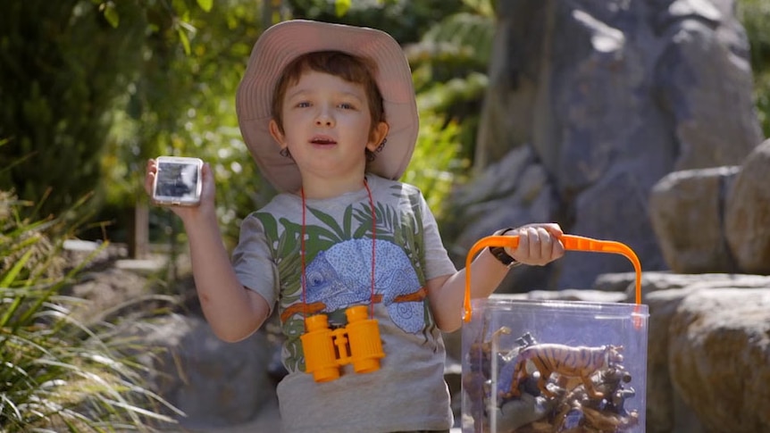 boy holding up phone in one hand and container with toy animals in the other