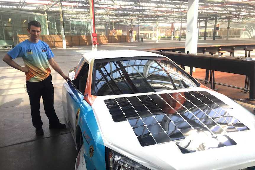 A man stands next to a solar-powered car.