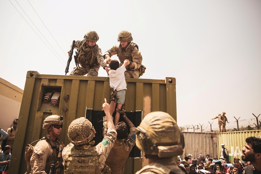 Two soldiers lift a small child by the arms up a wall 