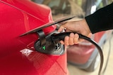 A hand holds an electric vehicle charging plug against a car.