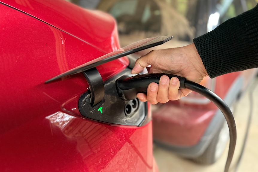 A hand holds an electric vehicle charging plug against a car