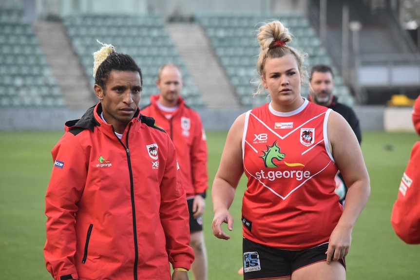 Elsie Albert wearing her red Dragons training gear stands on a football field with her teammates.