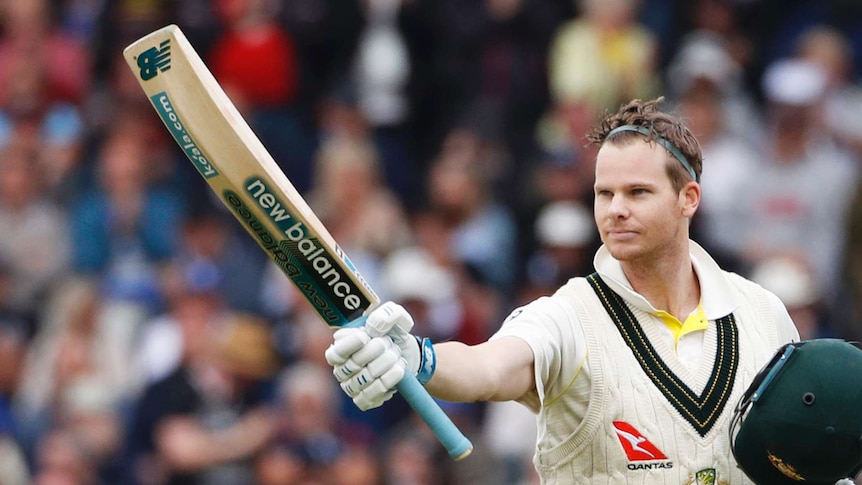 Steve Smith wearing a headband with helmet in hand raises his bat.