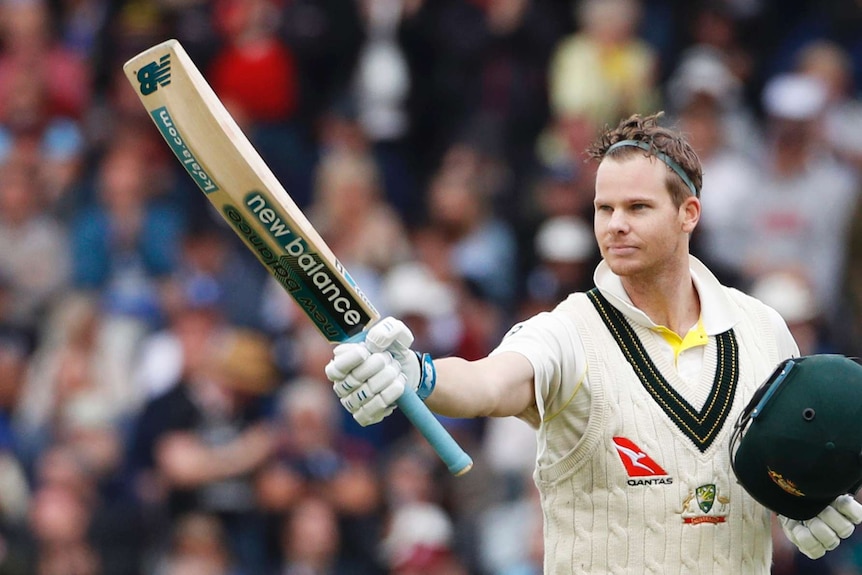 Steve Smith wearing a headband with helmet in hand raises his bat.