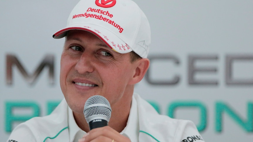 Michael Schumacher wearing a white hate speaks into a microphone during a press conference in 2012