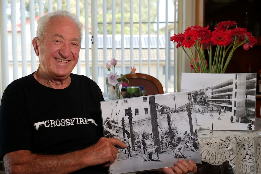 A man holds a large black and white photograph of a construction site