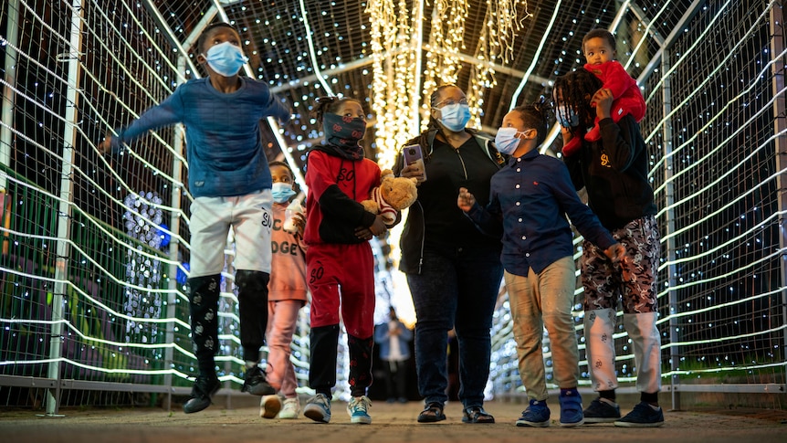 A woman and six children wearing face masks walk through a light tunnel in a South African city zoo