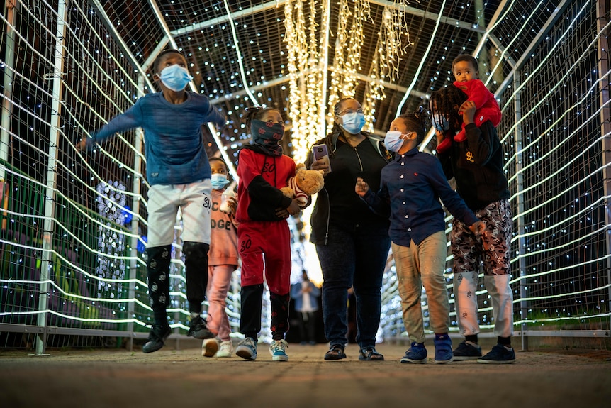A woman and six children wearing face masks walk through a light tunnel in a South African city zoo