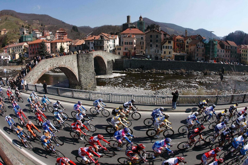 Bicycle riders ride on a road next to a river in the Milan San Remo cycle race