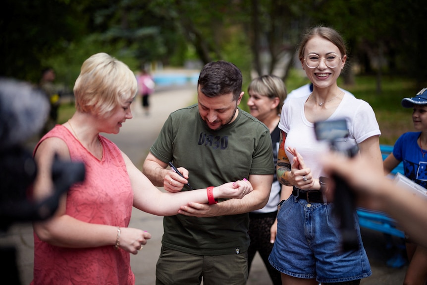 Volodymyr Zelenksyy signs a woman's arm.