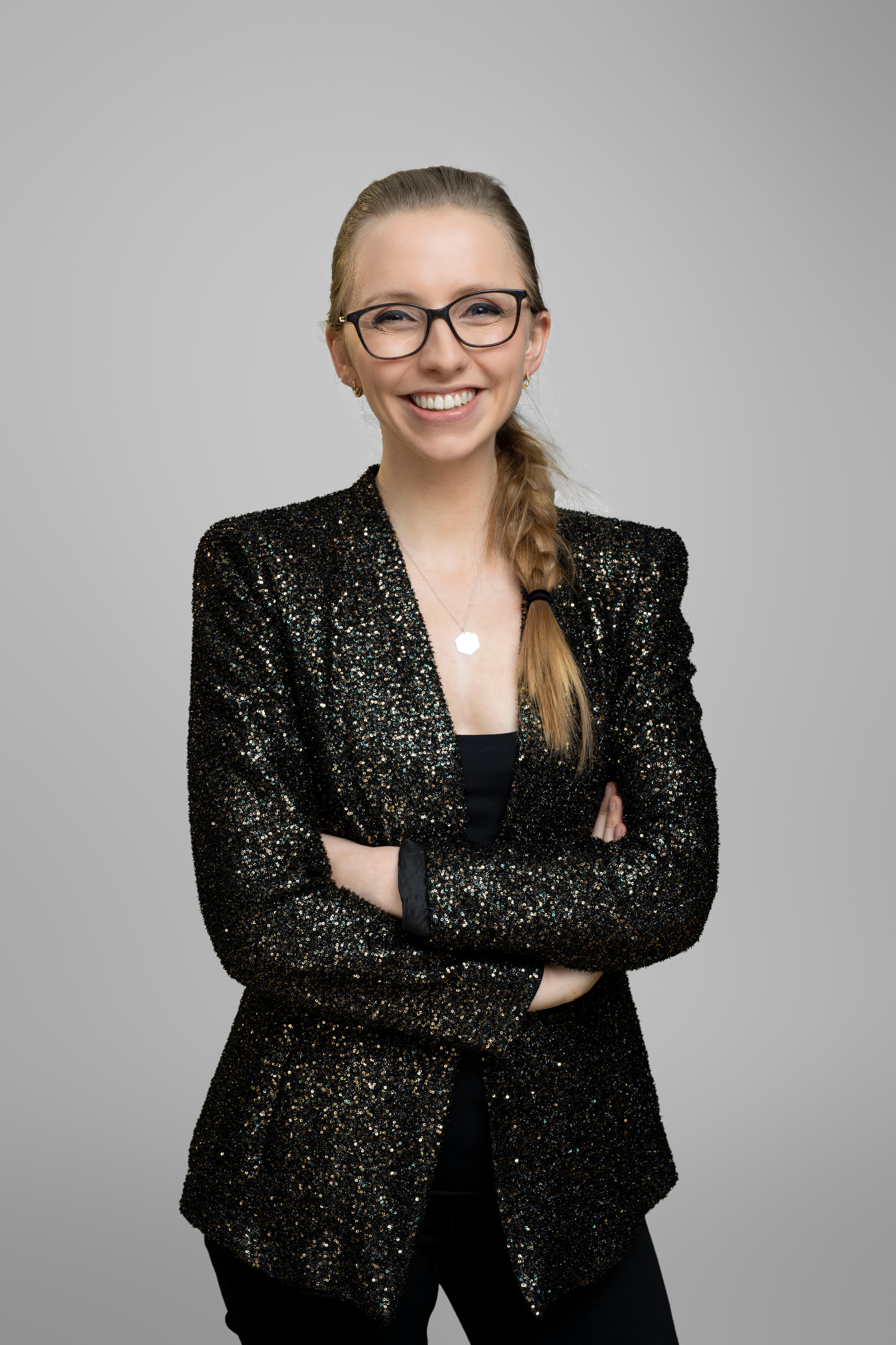 Anna Lapwood smiles at camera. She wears a black, sequined blazer and her hair is in a long  braid over her shoulder.