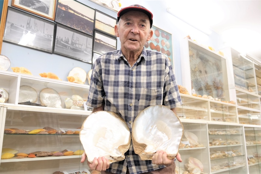 Neil Baker holds two pearl shells, with more shells and shelves in the background. 