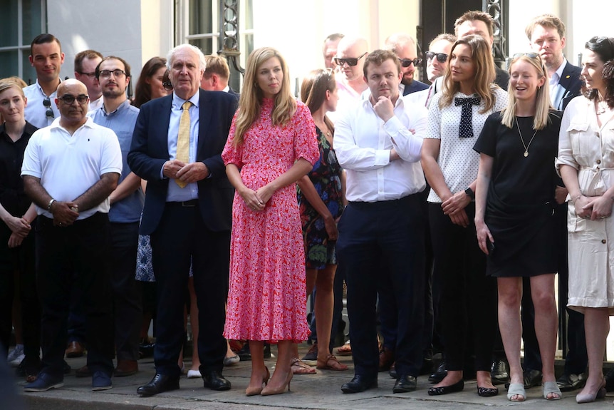 Boris Johnson's girlfriend, Carrie Symonds, wears a red flower patterned dress at the centre of a crowd outside Downing Street.