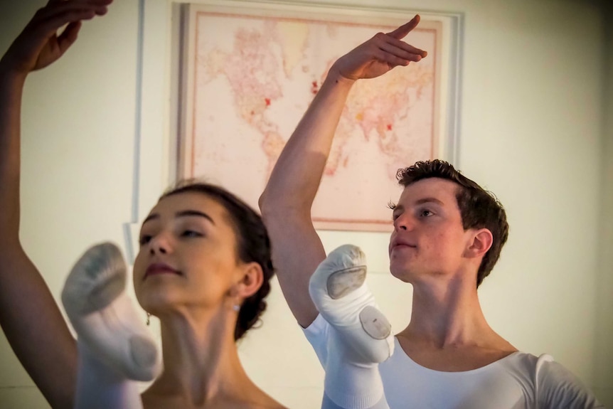 A young man and woman post during ballet practice.