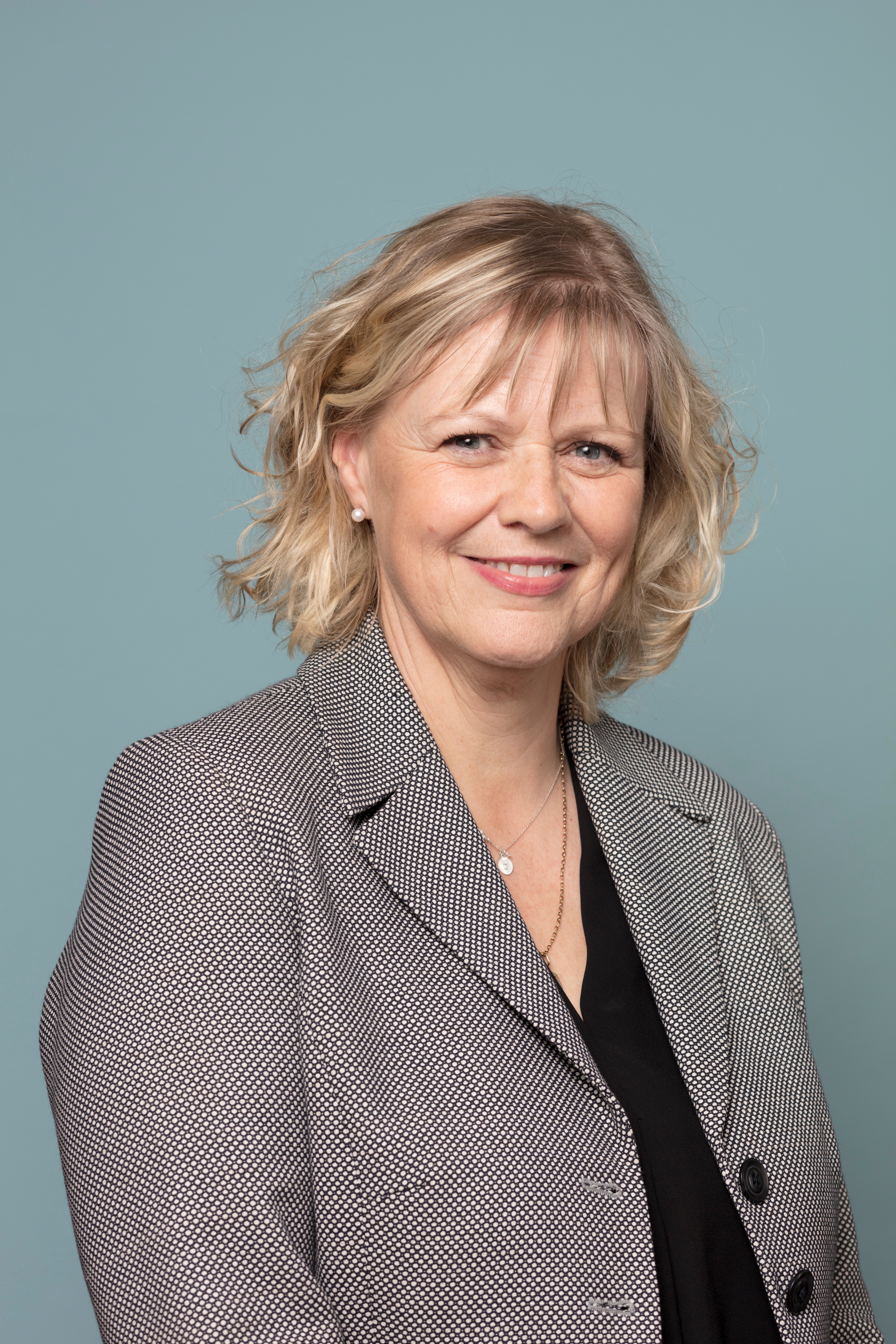 A woman in a grey blazer smiling in front of a grey background