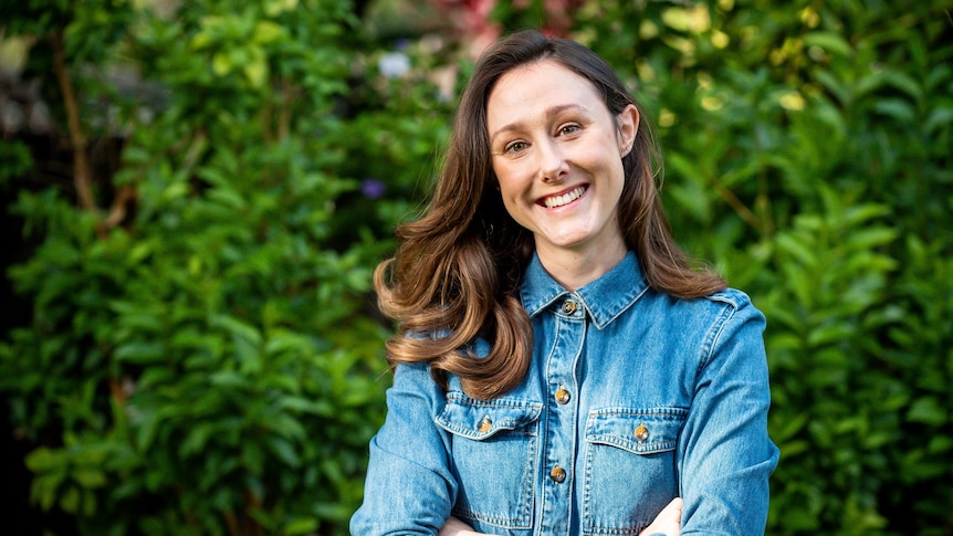 A woman stands in a garden smiling, in a story about trying cold showers for its benefits.