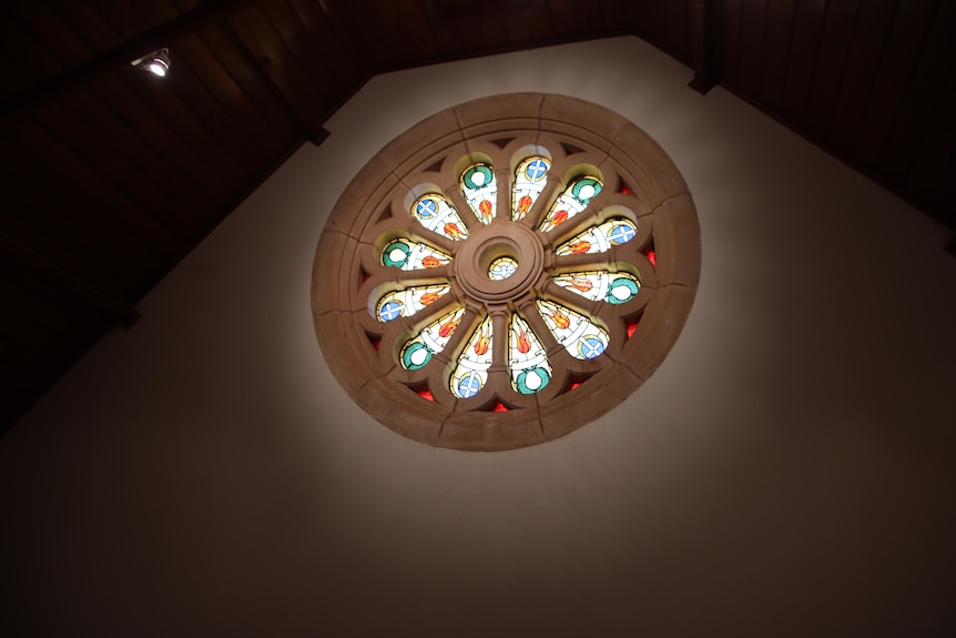 A multi-coloured circular stained glass window in a dark room.