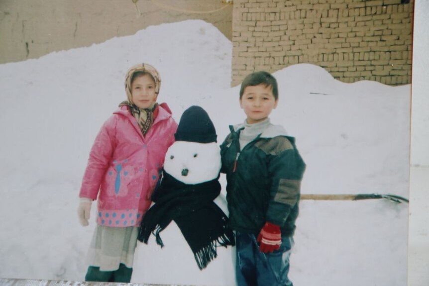 Two young children dressed in winter clothes next to a snowman