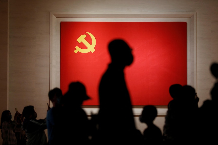 游客的身影映衬着中国共产党的党旗