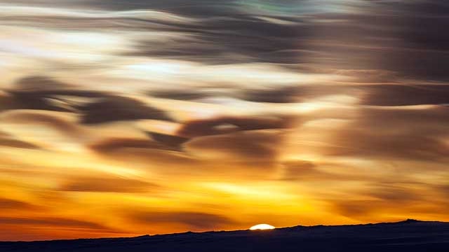 Beautiful wisps of stratospheric clouds over Antarctica with the sun on the horizon
