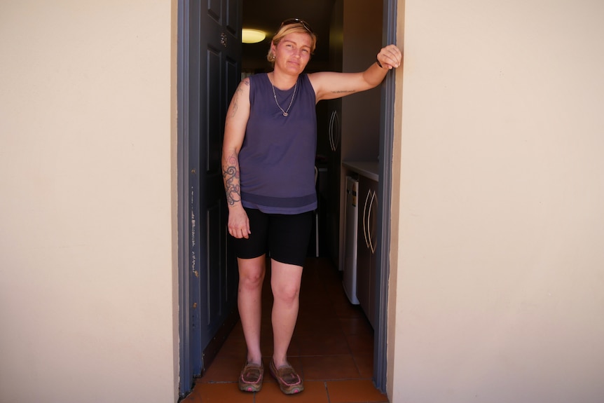 A woman stands in the open doorway of a motel with her arm resting on the wall