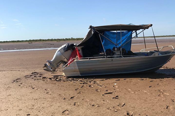A tinny boat with a shade sitting on a dry sand bed.
