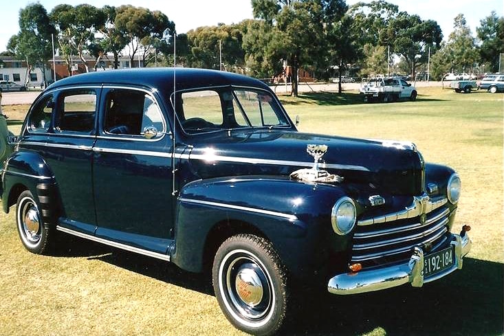 A historic blue sedan sits on a lawn.