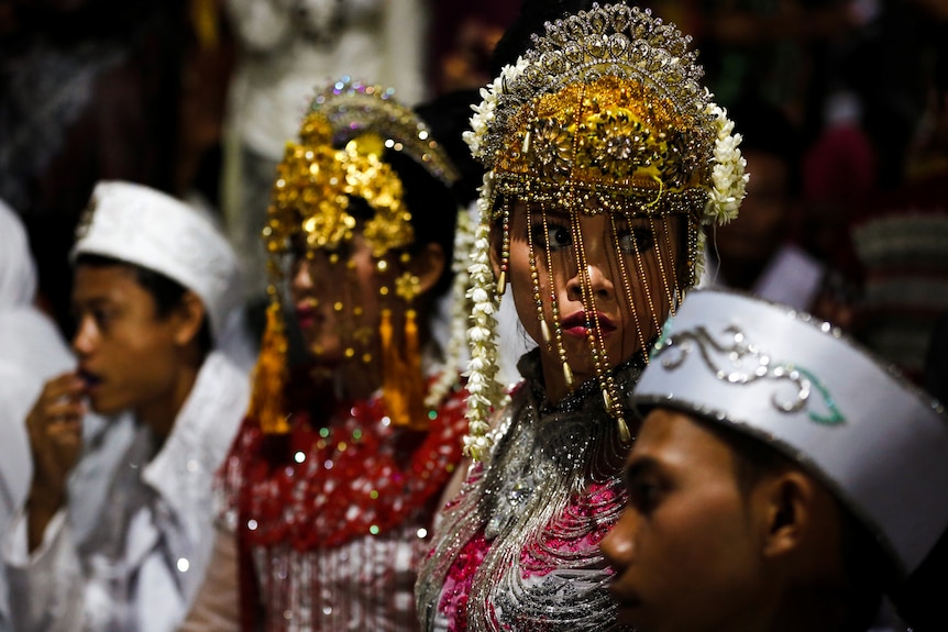 Two women wearing beaded head coverings stand in a line with two men on either side.
